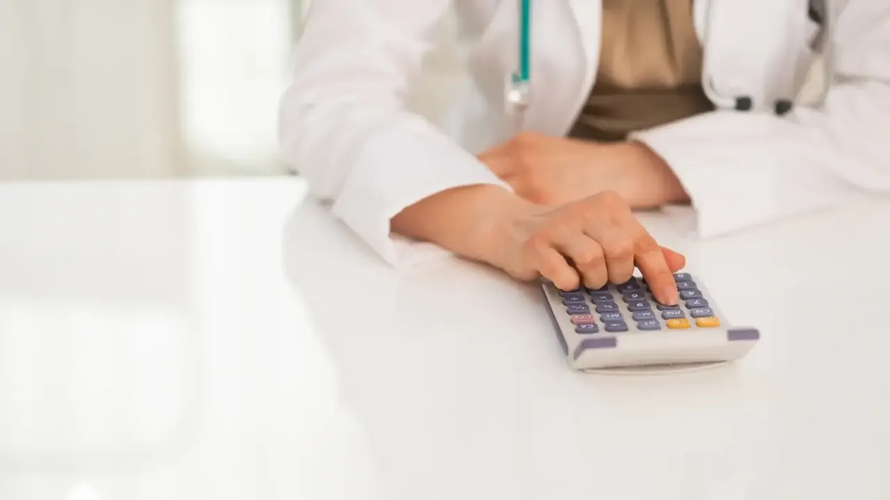 Uma médica em seu consultório fazendo as contas de suas finanças.
