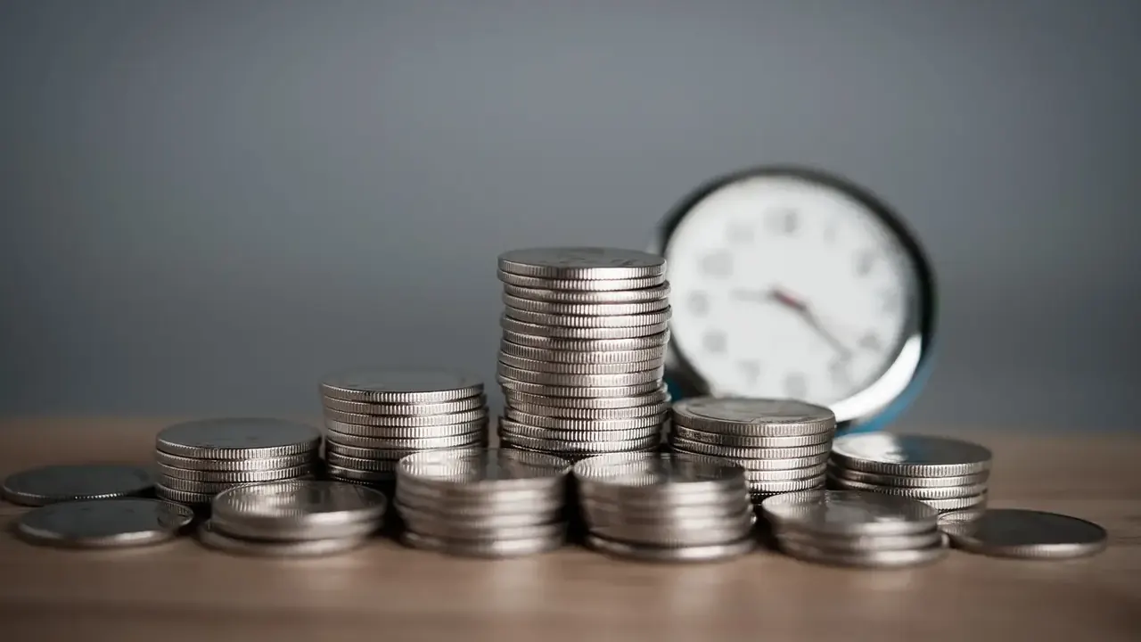 Várias pilhas de moedas e um relógio do lado